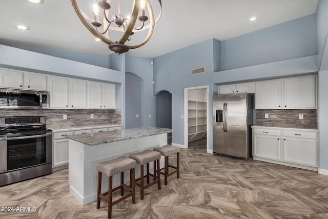 kitchen with light stone counters, appliances with stainless steel finishes, a kitchen island, and white cabinetry