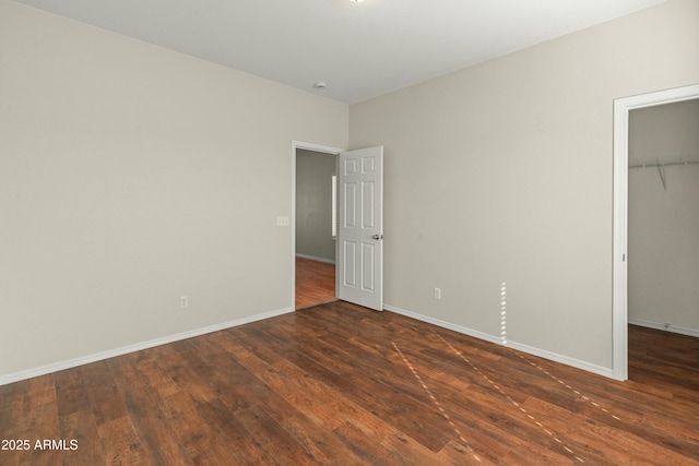 unfurnished bedroom with dark wood-type flooring, a spacious closet, and a closet