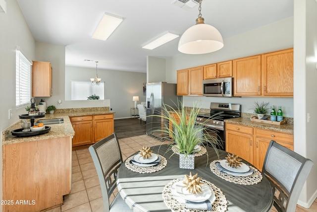 kitchen with hanging light fixtures, light tile patterned flooring, appliances with stainless steel finishes, and light stone countertops