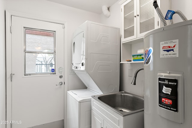 laundry room featuring electric water heater, a sink, stacked washer and clothes dryer, and cabinet space