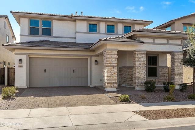 prairie-style house featuring stone siding, a tile roof, an attached garage, decorative driveway, and stucco siding