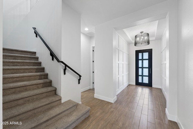 foyer featuring stairway, an inviting chandelier, wood finished floors, and baseboards