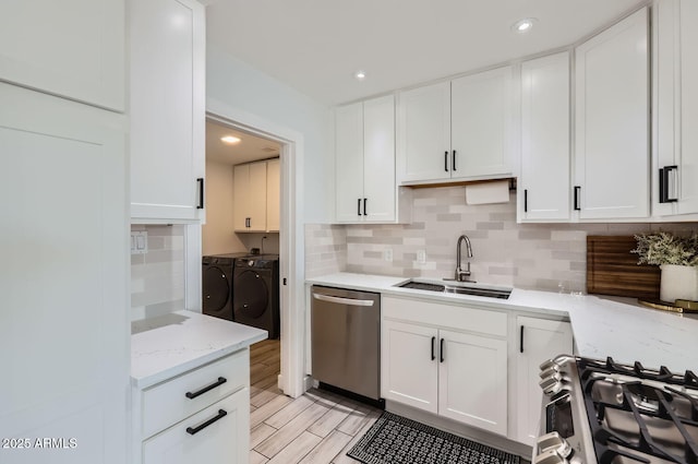 kitchen with range with gas stovetop, white cabinetry, dishwasher, sink, and washing machine and clothes dryer