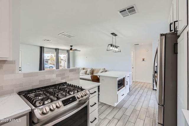 kitchen featuring ceiling fan, appliances with stainless steel finishes, a center island, white cabinets, and decorative backsplash