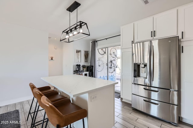 kitchen featuring stainless steel refrigerator with ice dispenser, white cabinetry, light stone counters, decorative light fixtures, and a center island