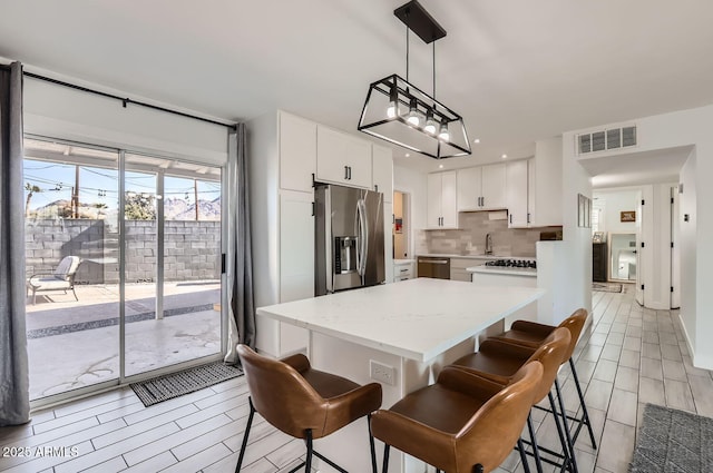 kitchen with appliances with stainless steel finishes, a breakfast bar, decorative light fixtures, tasteful backsplash, and white cabinets