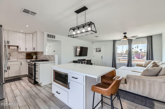 kitchen featuring light stone counters, pendant lighting, stainless steel appliances, decorative backsplash, and white cabinets