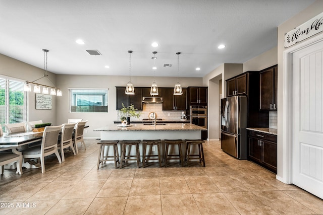 kitchen featuring decorative backsplash, a kitchen breakfast bar, light stone countertops, stainless steel appliances, and under cabinet range hood