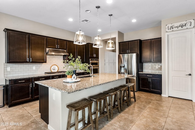 kitchen featuring under cabinet range hood, stainless steel appliances, a sink, visible vents, and a kitchen breakfast bar