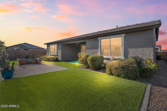 back house at dusk with a lawn and a patio area