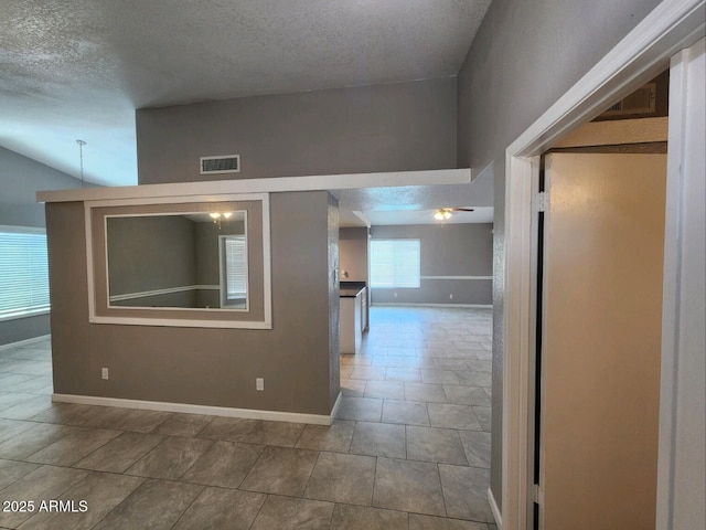 corridor featuring tile patterned flooring, lofted ceiling, and a textured ceiling