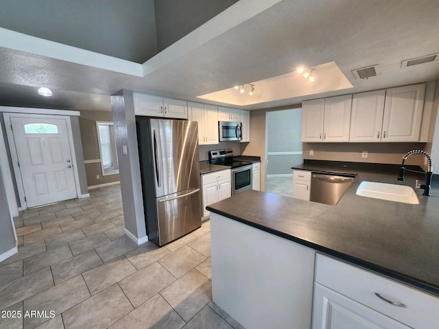 kitchen with sink, a raised ceiling, light tile patterned flooring, white cabinets, and appliances with stainless steel finishes