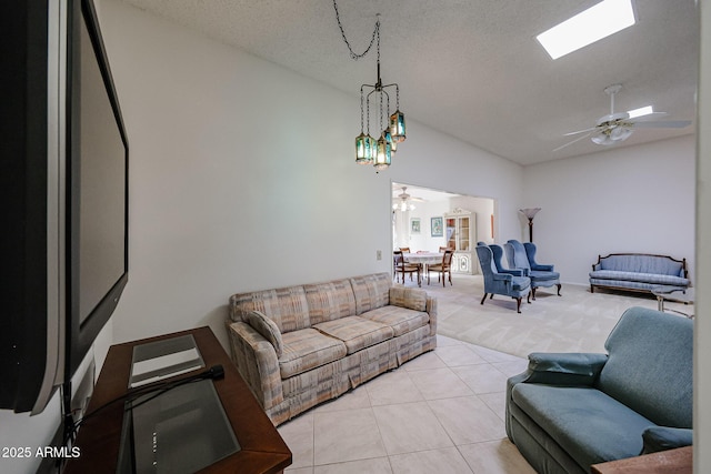 tiled living room with vaulted ceiling with skylight, a textured ceiling, and ceiling fan