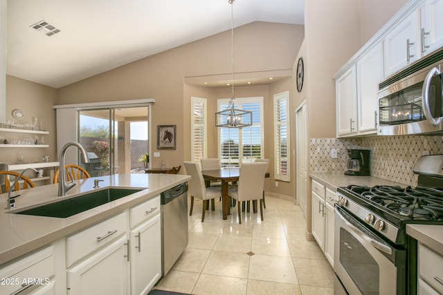 kitchen featuring lofted ceiling, sink, white cabinetry, decorative light fixtures, and appliances with stainless steel finishes