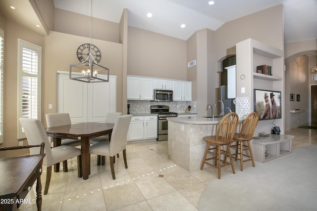 kitchen featuring white cabinetry, tasteful backsplash, hanging light fixtures, light tile patterned floors, and stainless steel appliances