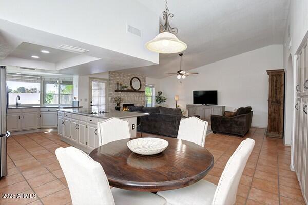 dining space with a fireplace, lofted ceiling, sink, light tile patterned floors, and ceiling fan