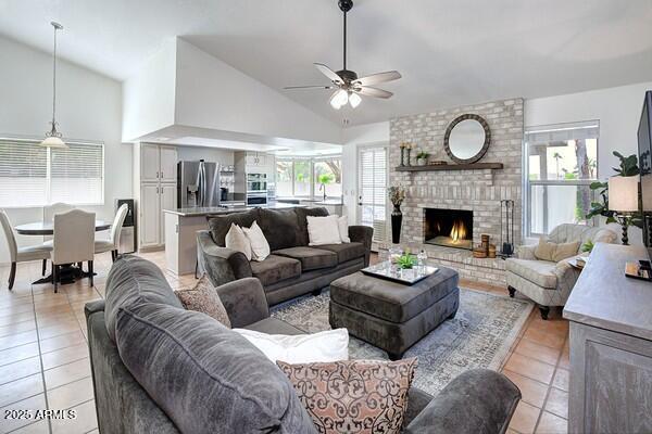 living room featuring ceiling fan, a healthy amount of sunlight, a brick fireplace, and light tile patterned floors