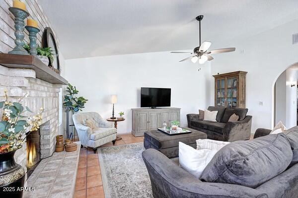 living room with ceiling fan, lofted ceiling, a brick fireplace, and light tile patterned floors