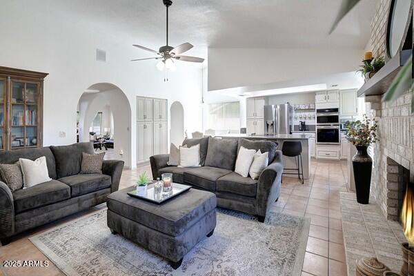 tiled living room with a brick fireplace, high vaulted ceiling, and ceiling fan