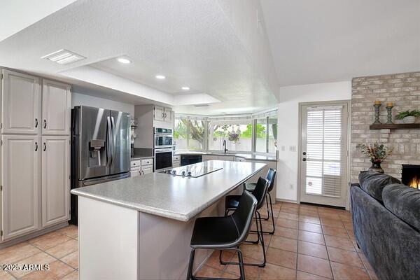 kitchen featuring stainless steel appliances, a breakfast bar, a center island, a raised ceiling, and a healthy amount of sunlight