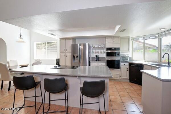 kitchen with pendant lighting, black appliances, white cabinetry, sink, and a tray ceiling