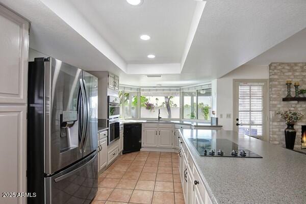 kitchen with sink, a tray ceiling, black appliances, white cabinets, and light tile patterned flooring