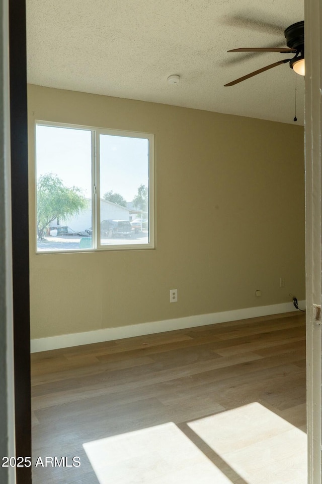 spare room with baseboards, a ceiling fan, wood finished floors, and a textured ceiling