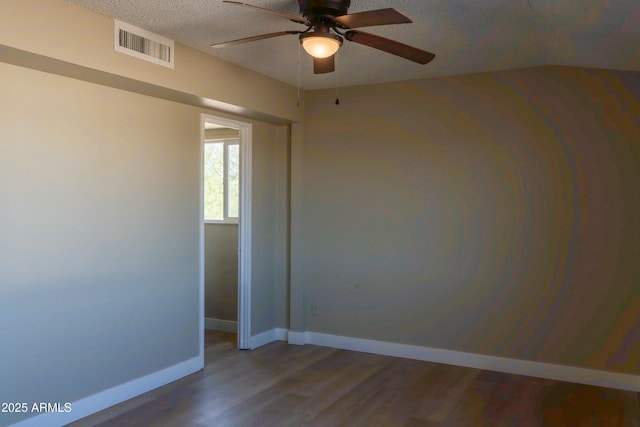empty room featuring a textured ceiling, baseboards, visible vents, a ceiling fan, and wood finished floors