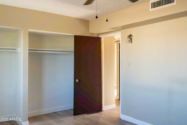 unfurnished bedroom with baseboards, wood finished floors, a textured ceiling, and visible vents