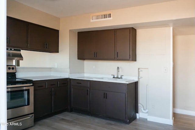 kitchen featuring light wood finished floors, under cabinet range hood, visible vents, a sink, and electric range