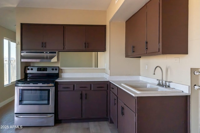 kitchen featuring a sink, stainless steel electric range oven, light wood-type flooring, light countertops, and under cabinet range hood
