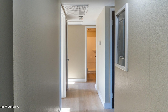 hall with a textured wall, wood finished floors, and visible vents