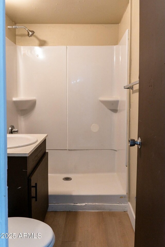 bathroom featuring a shower stall, toilet, vanity, and wood finished floors