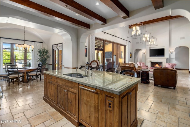 kitchen featuring hanging light fixtures, a kitchen island with sink, beam ceiling, a notable chandelier, and sink