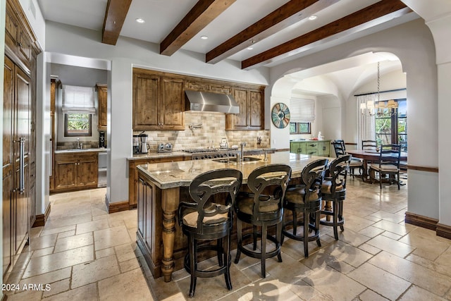 kitchen with plenty of natural light, a kitchen island with sink, wall chimney exhaust hood, and decorative light fixtures