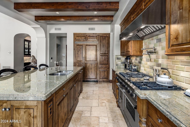 kitchen with backsplash, beam ceiling, wall chimney exhaust hood, sink, and light tile floors