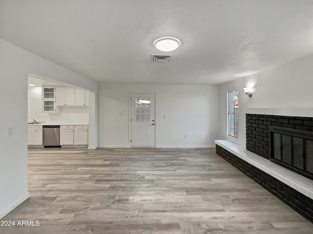 unfurnished living room with sink, light wood-type flooring, and a brick fireplace