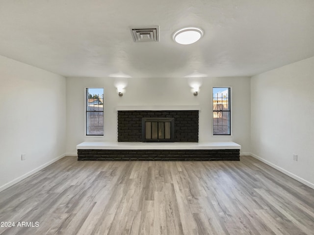 unfurnished living room with light wood-type flooring and a brick fireplace