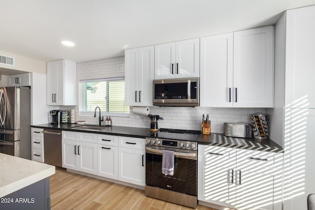 kitchen with decorative backsplash, appliances with stainless steel finishes, sink, light hardwood / wood-style flooring, and white cabinets