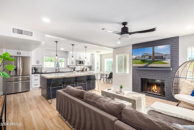 living room featuring ceiling fan, light hardwood / wood-style flooring, sink, and a brick fireplace