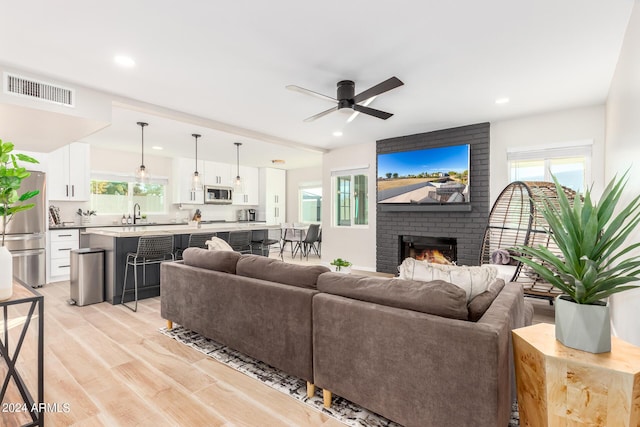 living room with ceiling fan, a fireplace, and light hardwood / wood-style flooring