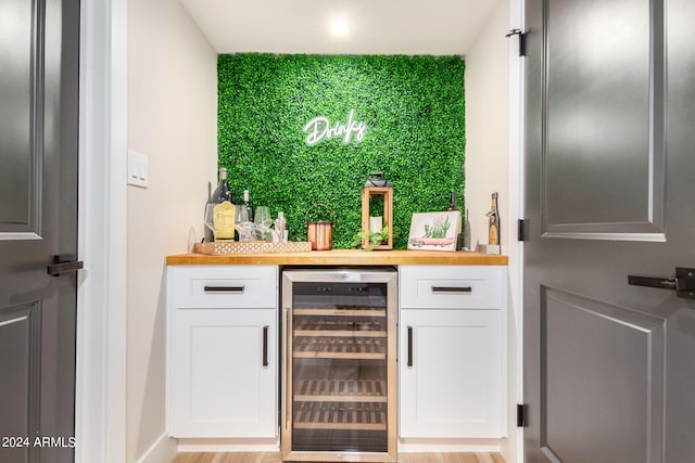 bar featuring wine cooler, white cabinetry, light hardwood / wood-style floors, and wood counters