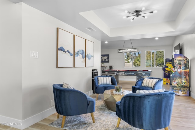 living area featuring a tray ceiling, light hardwood / wood-style flooring, and a notable chandelier