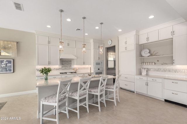 kitchen featuring backsplash, white appliances, a center island with sink, white cabinets, and a breakfast bar area