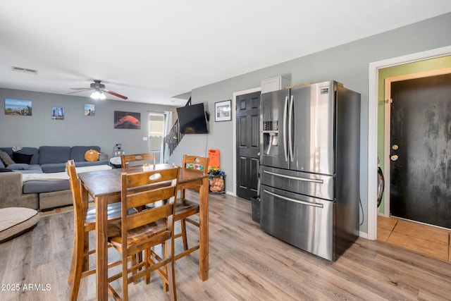 dining area with light wood-type flooring, visible vents, ceiling fan, and stairs