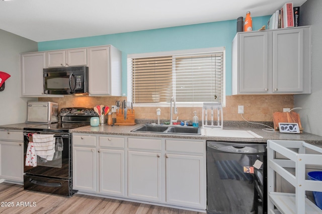 kitchen with black appliances, tasteful backsplash, light wood-type flooring, and a sink