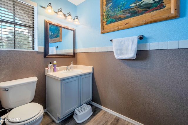 bathroom featuring baseboards, a textured wall, toilet, wood finished floors, and vanity