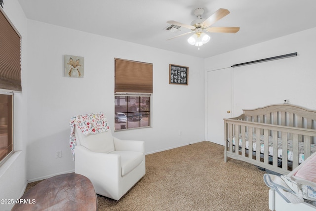 carpeted bedroom with a crib, ceiling fan, visible vents, and a closet