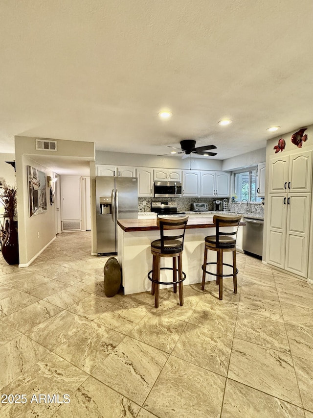 kitchen featuring tasteful backsplash, visible vents, a breakfast bar area, stainless steel appliances, and white cabinetry