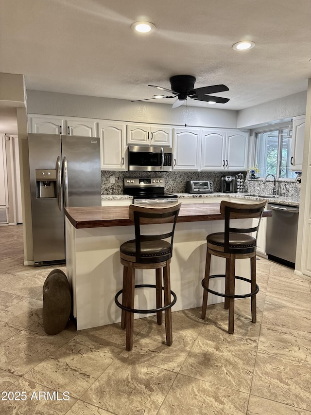 kitchen featuring white cabinets, a kitchen island, butcher block countertops, appliances with stainless steel finishes, and a kitchen breakfast bar